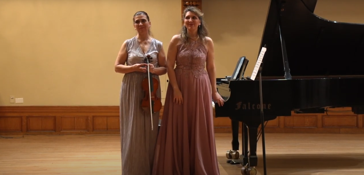 Two women standing next to each other after performing as a violin and piano duo.